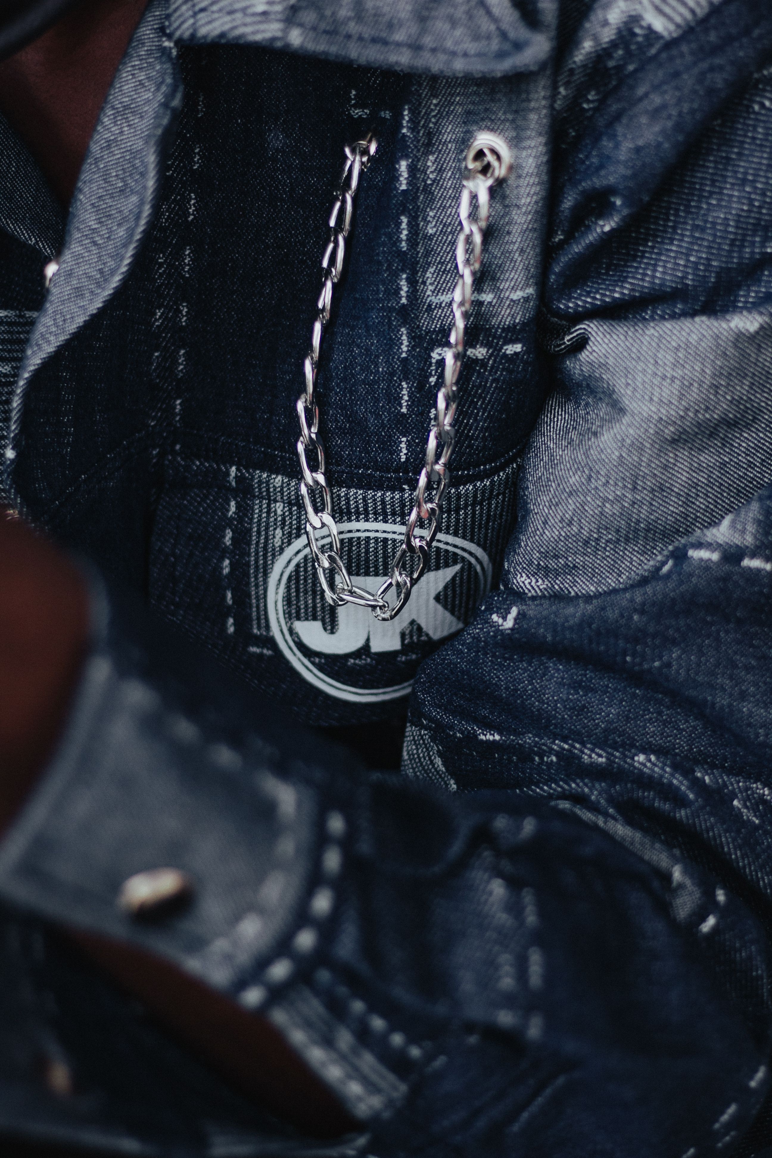 Detailed image of a denim jacket pocket with a silver chain hanging from it.