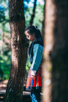 Fashionable woman with glasses amongst vibrant trees, showcasing street style.