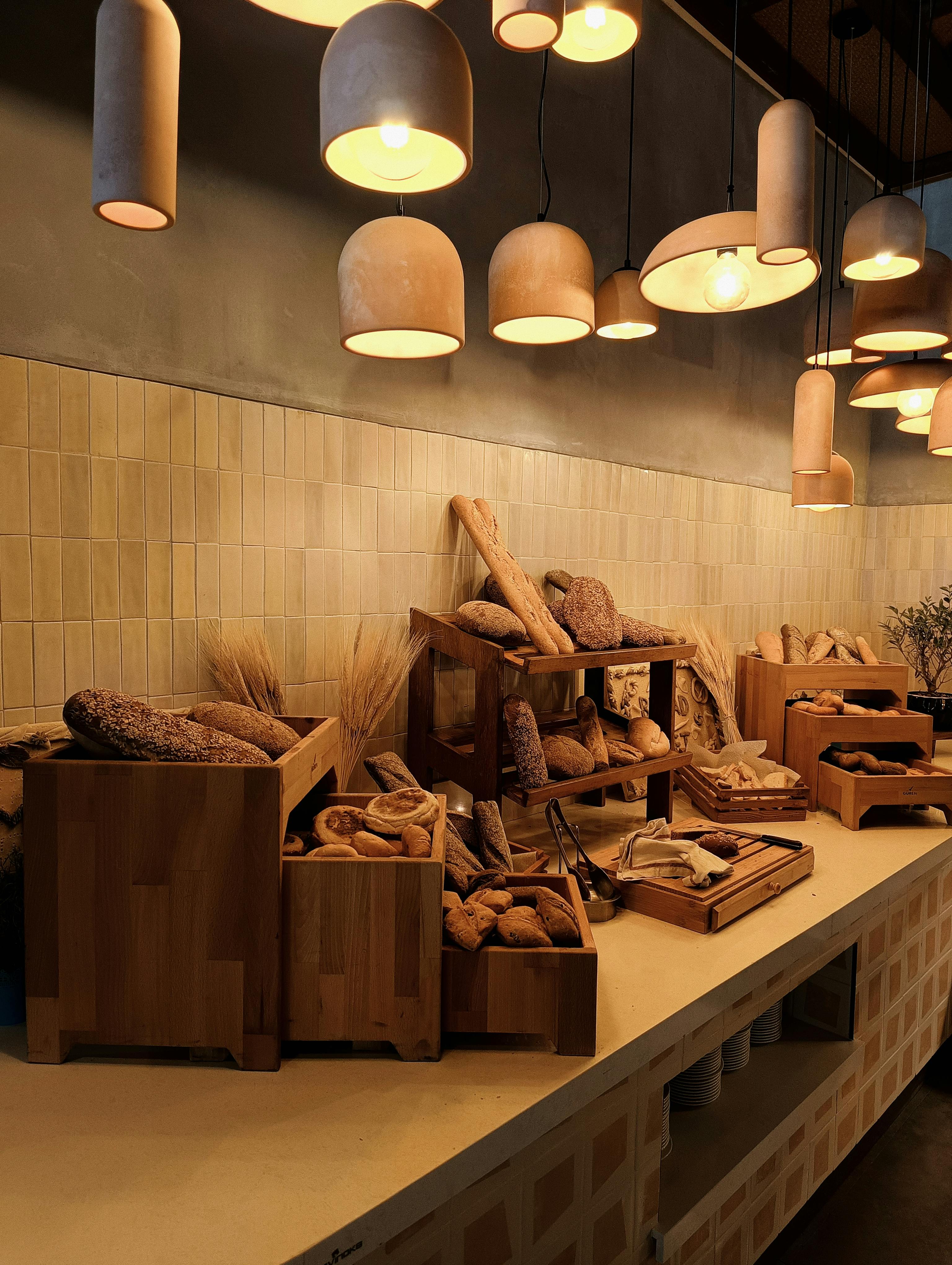 A rustic display of artisan breads illuminated by warm pendant lights in a cozy bakery setting.