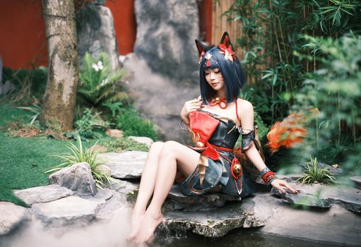 Female in cosplay costume poses in a tranquil Asian-inspired garden setting.