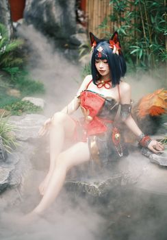 A cosplayer in an elaborate costume poses amidst mist in a serene forest landscape.
