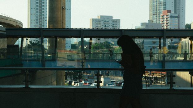 在城市景观、建筑物和交通的背景下，一个女人的剪影映在手机上