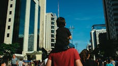 一位父亲扛着儿子，穿过高楼林立的繁华都市街道