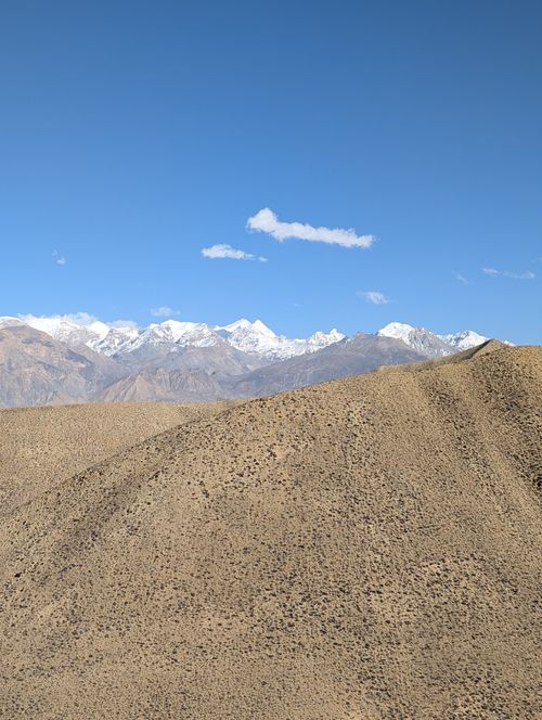 Free Sweeping view of snow-capped mountains against a clear blue sky with desert hills in the foreground. Stock Photo