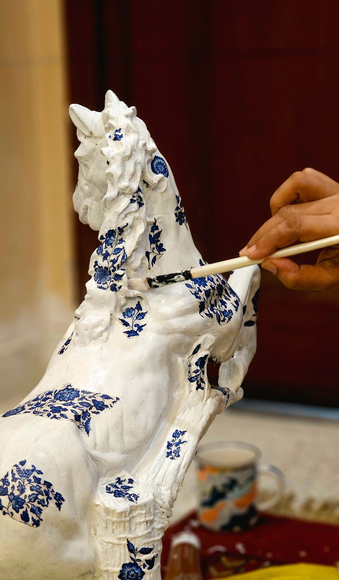 An artisan hand-painting blue floral patterns onto a glazed white ceramic piece
