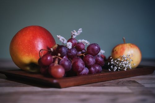 Free A classic still life of apples, grapes, and flowers on a wooden tray. Stock Photo
