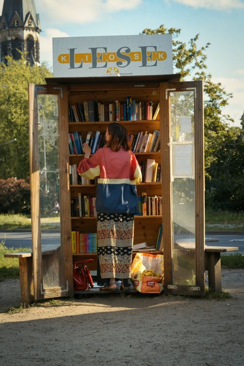 Free A woman exploring a small outdoor book exchange in Berlin during a sunny day. Stock Photo