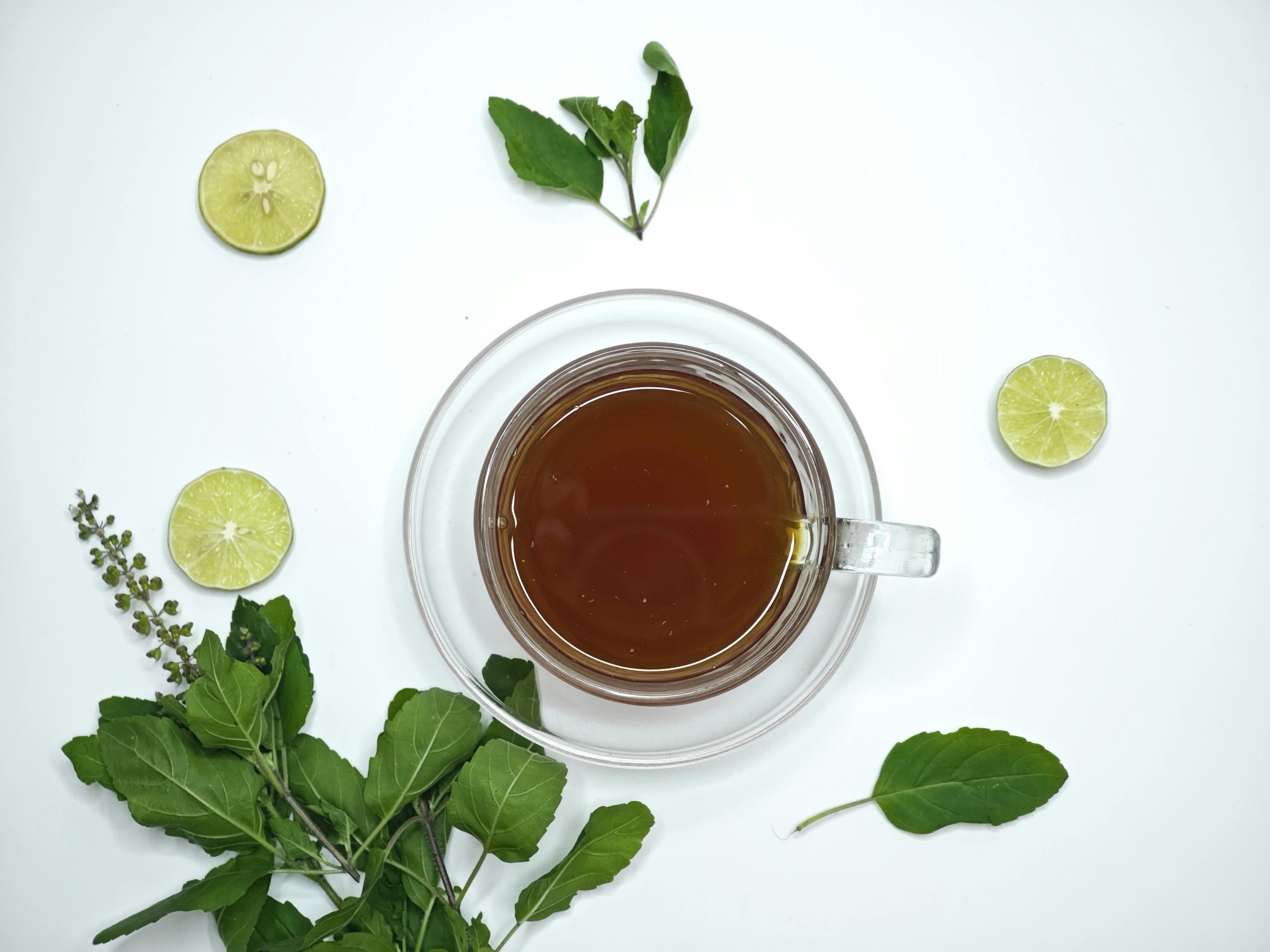 A cup of aromatic tulsi tea surrounded by fresh lime slices and basil leaves, offering a refreshing herbal beverage.