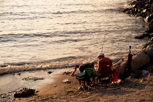 Two people fishing on a rocky beach at sunset, creating a tranquil and relaxing atmosphere.