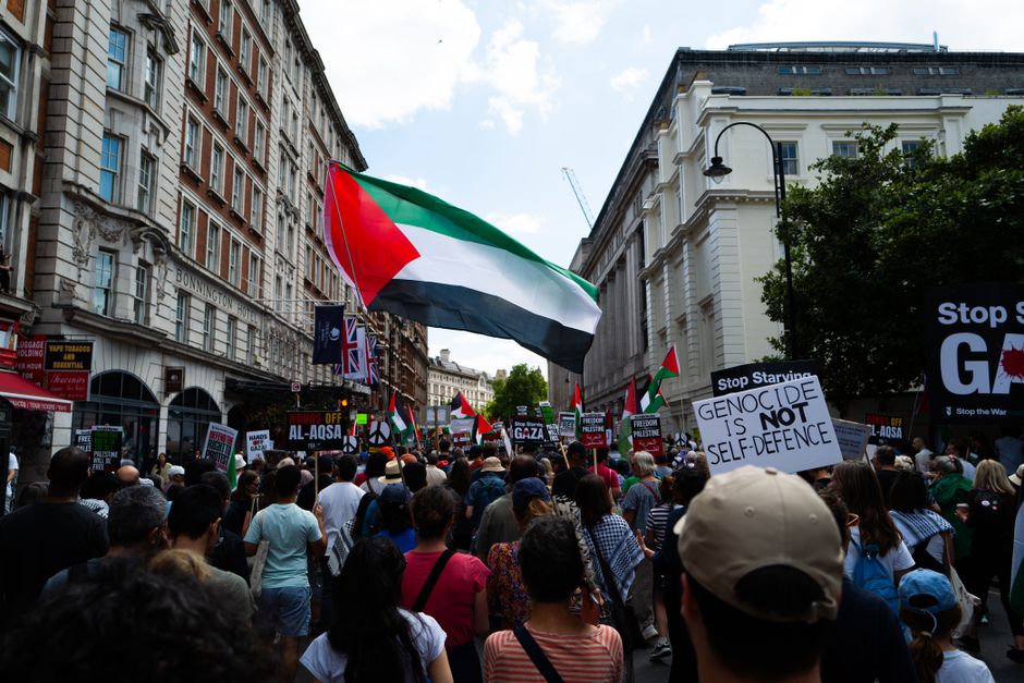 Crowd in London protests for Palestinian rights, waving flags and holding signs.