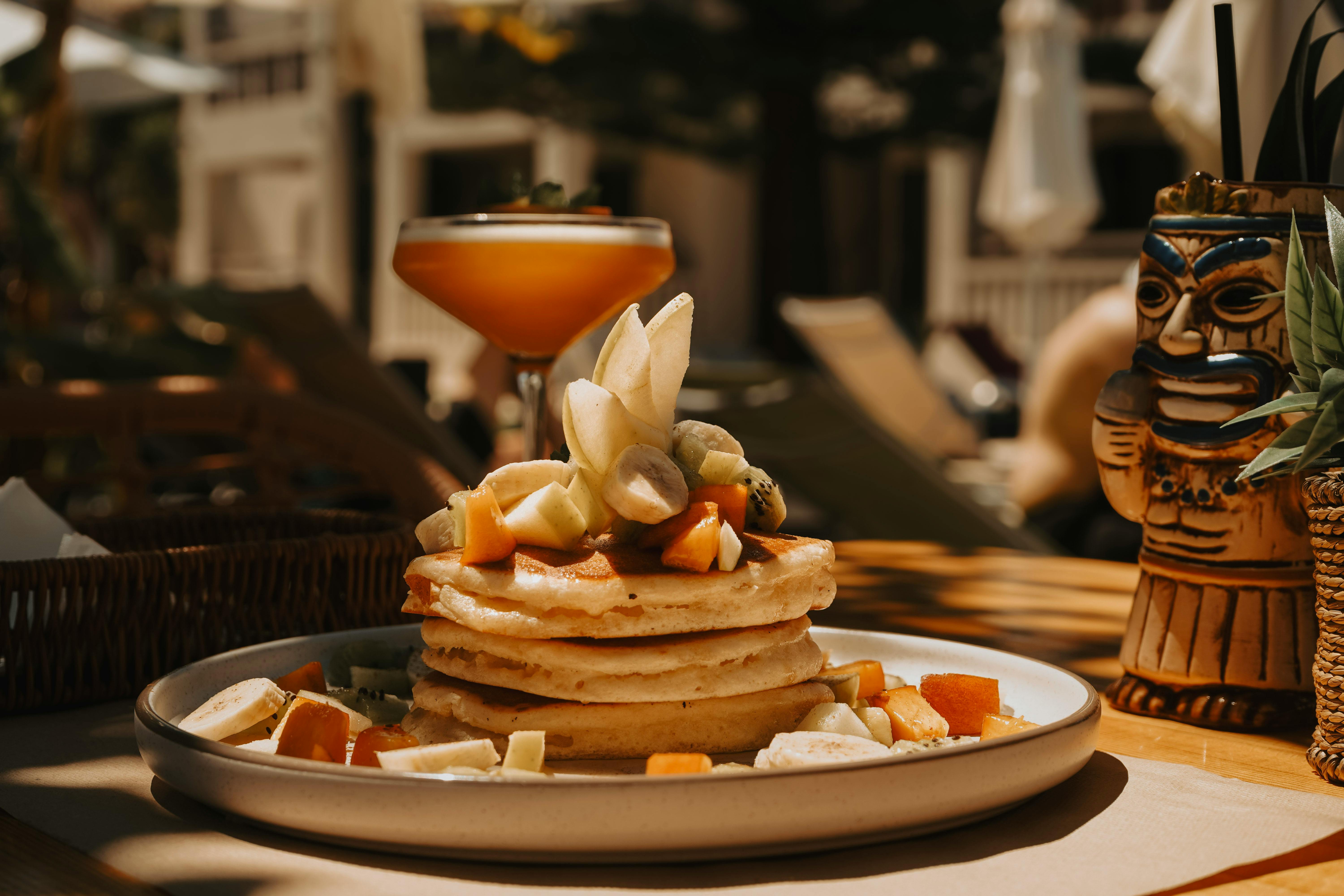 Free Stack of pancakes with fresh tropical fruits and cocktail set in a sunny outdoor cafe. Stock Photo