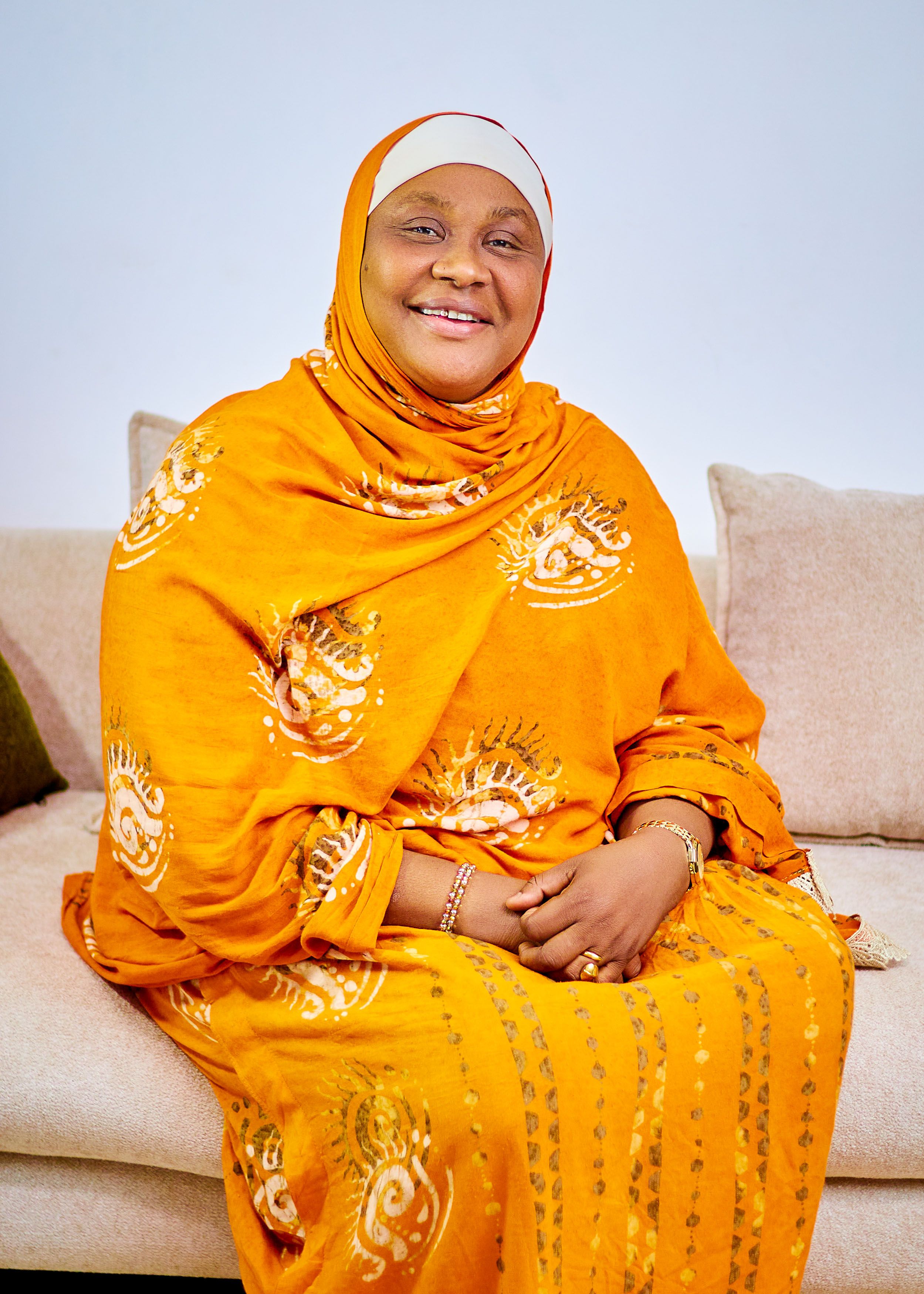 Portrait of a cheerful woman in vibrant orange traditional clothing sitting on a couch.