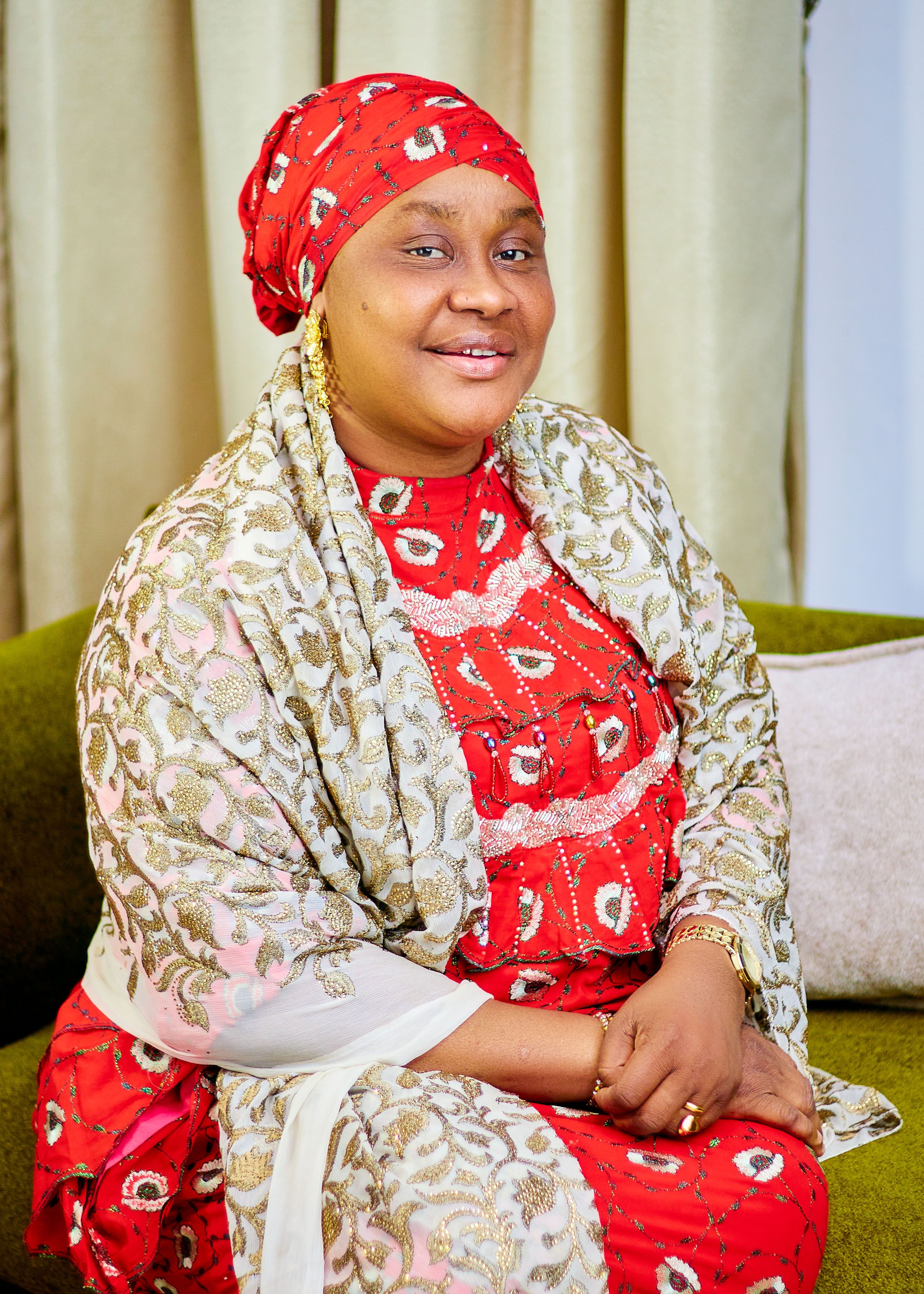 A confident woman in vibrant traditional attire, sitting indoors.