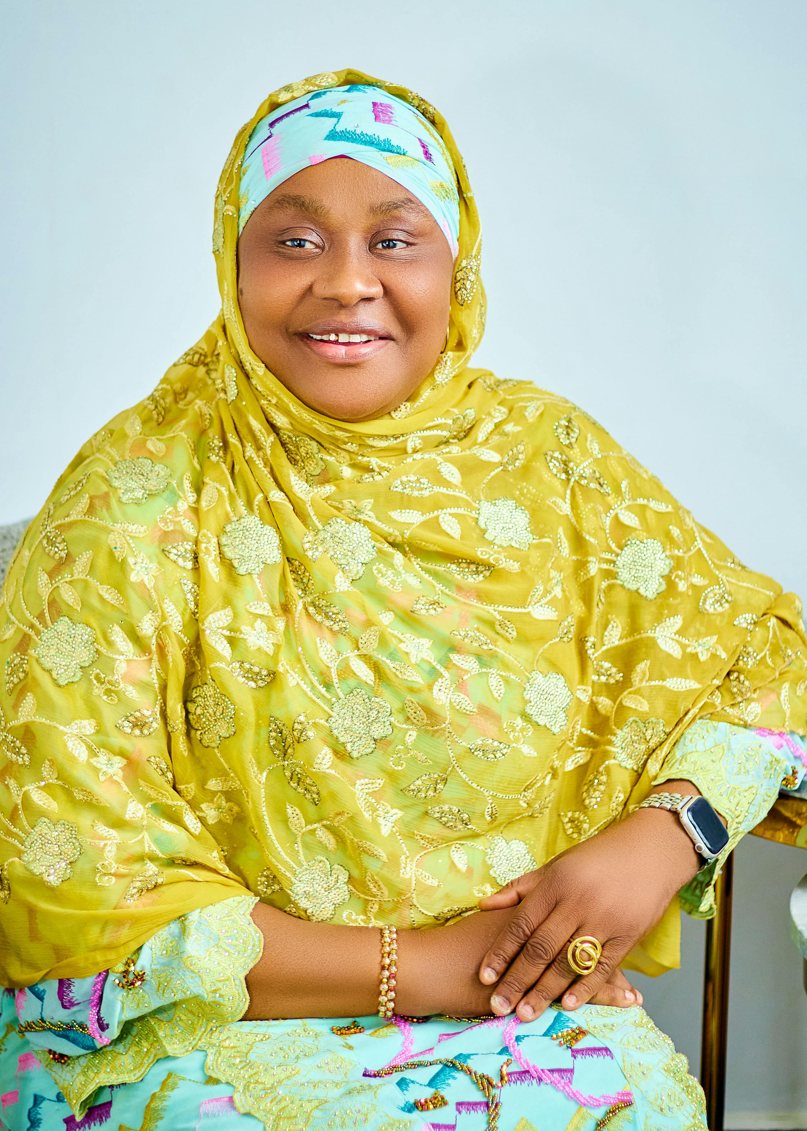 A cheerful African woman in a vibrant hijab poses in a bright setting.
