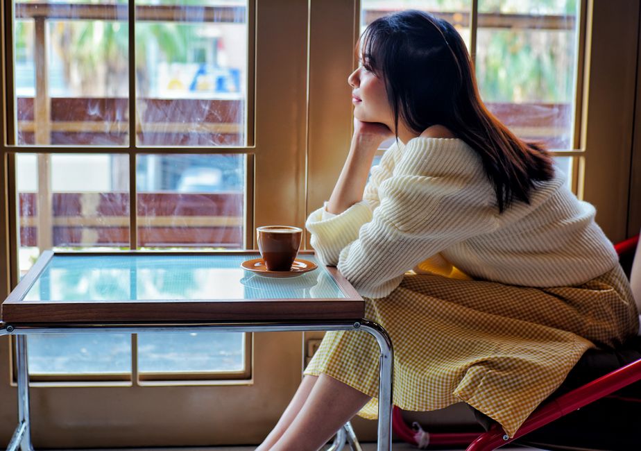 Woman in a cozy setting enjoys coffee by the window, gazing outside, indoors.