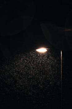 Atmospheric scene of raindrops illuminated by a street lamp at night, creating a serene mood.
