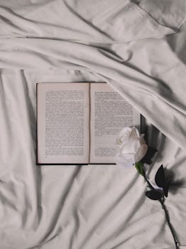 Aesthetic composition of an open book and white rose on soft fabric background, embodying tranquility.