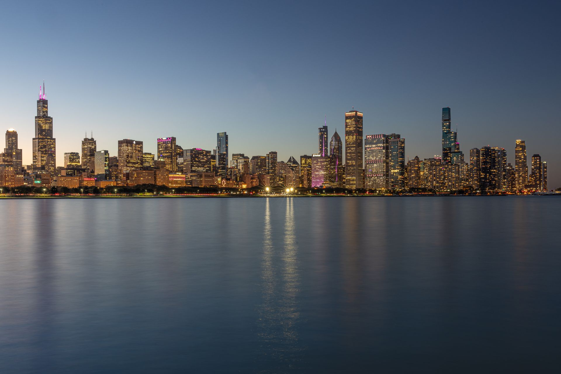 Chicago skyline at dusk with illuminated buildings reflected in Lake Michigan