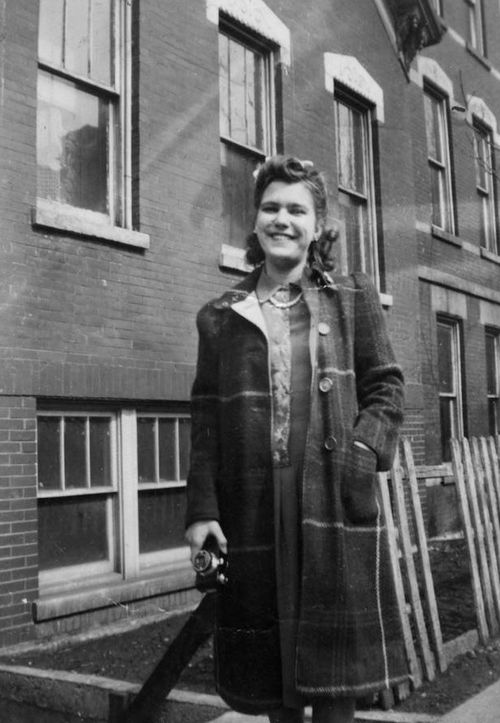 Free Black and white photo of a smiling woman in 1940s winter fashion holding a camera. Stock Photo