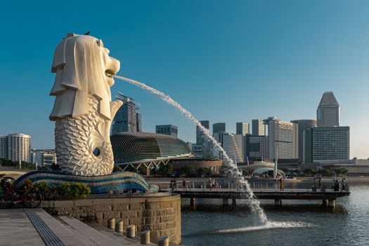 Iconic Merlion statue with Singapore skyline under clear blue sky, showcasing modern architecture and city's charm.