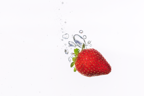 Free A vibrant strawberry making a splash in clear water, captured in mid-air with perfect clarity. Stock Photo