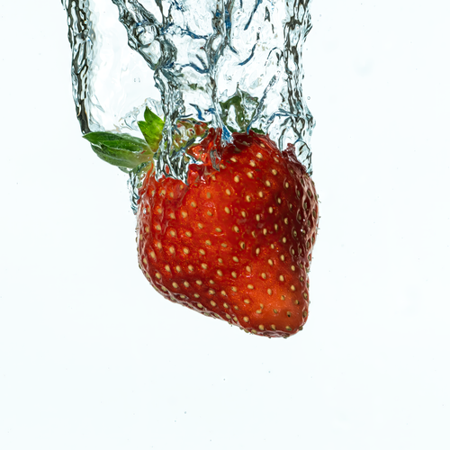 Free A fresh strawberry captured in mid-air as it splashes into water creating dynamic motion. Stock Photo