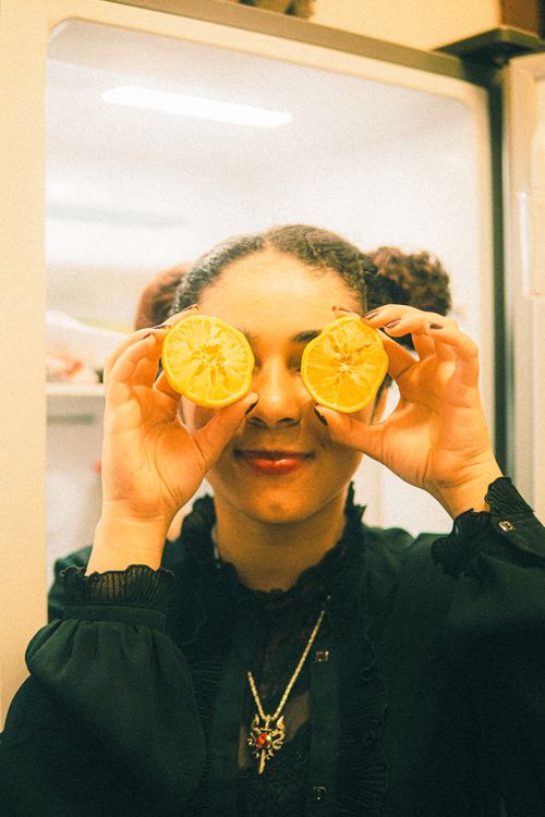 Free Adult woman in kitchen using orange slices as glasses, creating a playful and fun atmosphere. Stock Photo
