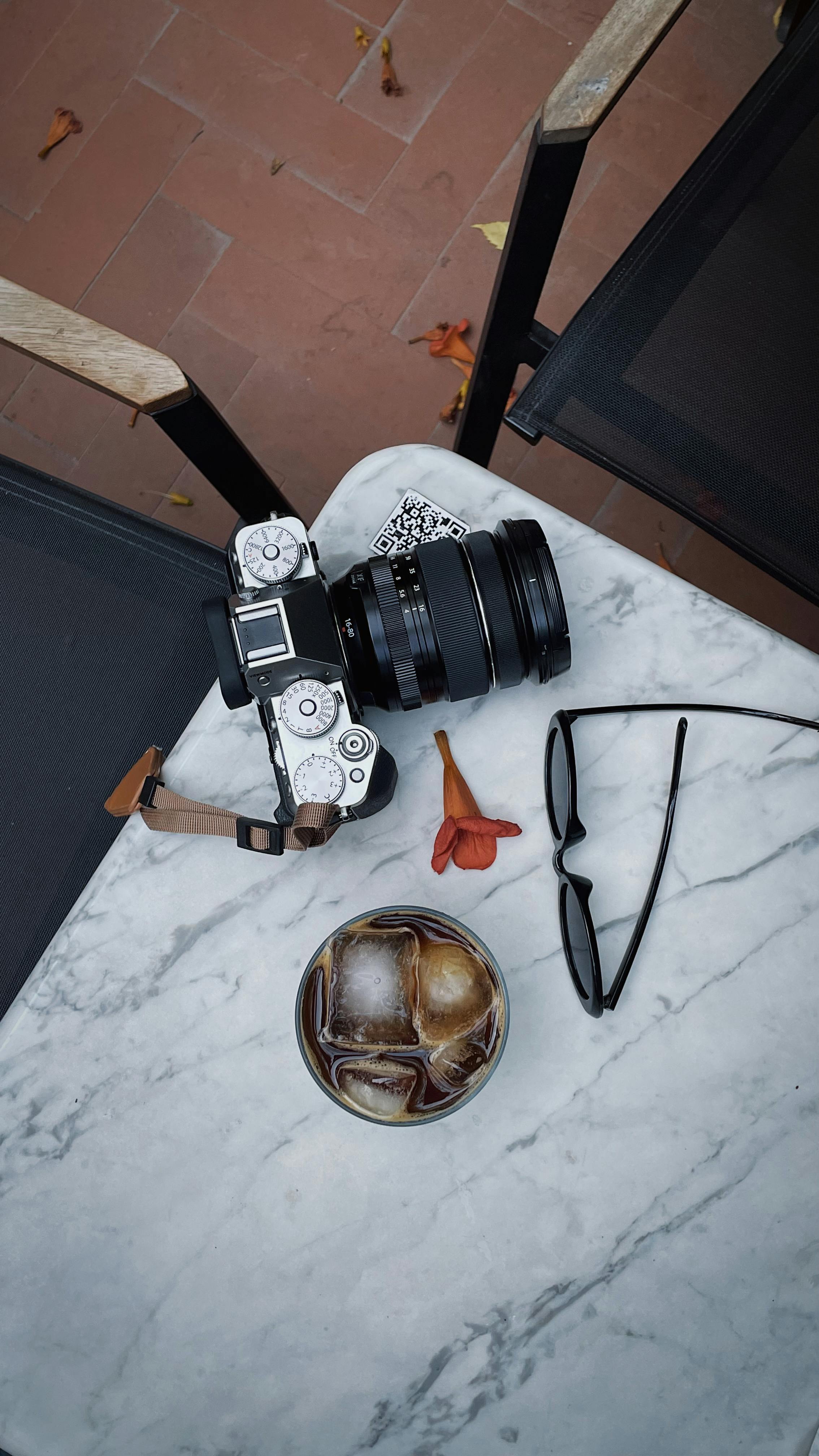 A modern flat lay image featuring a camera, iced coffee, and sunglasses on a marble table.