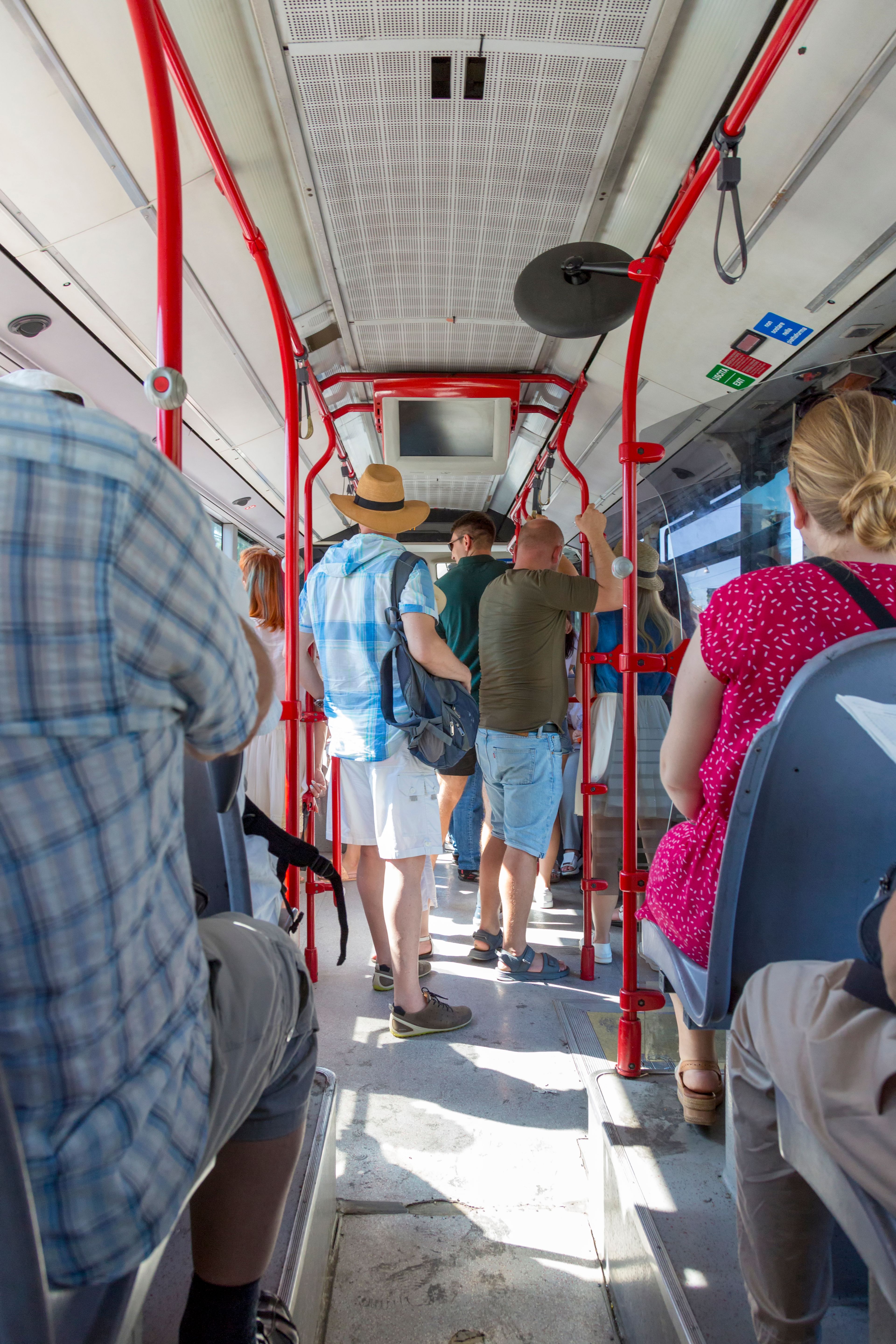 Un grupo diverso de personas de pie dentro de un autobús urbano durante el día.