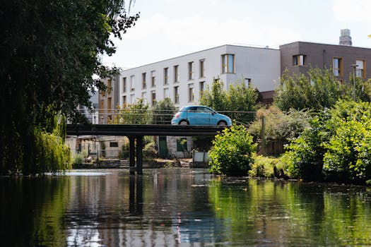A tranquil canal scene in France featuring a car crossing a bridge, surrounded by lush greenery and modern buildings.