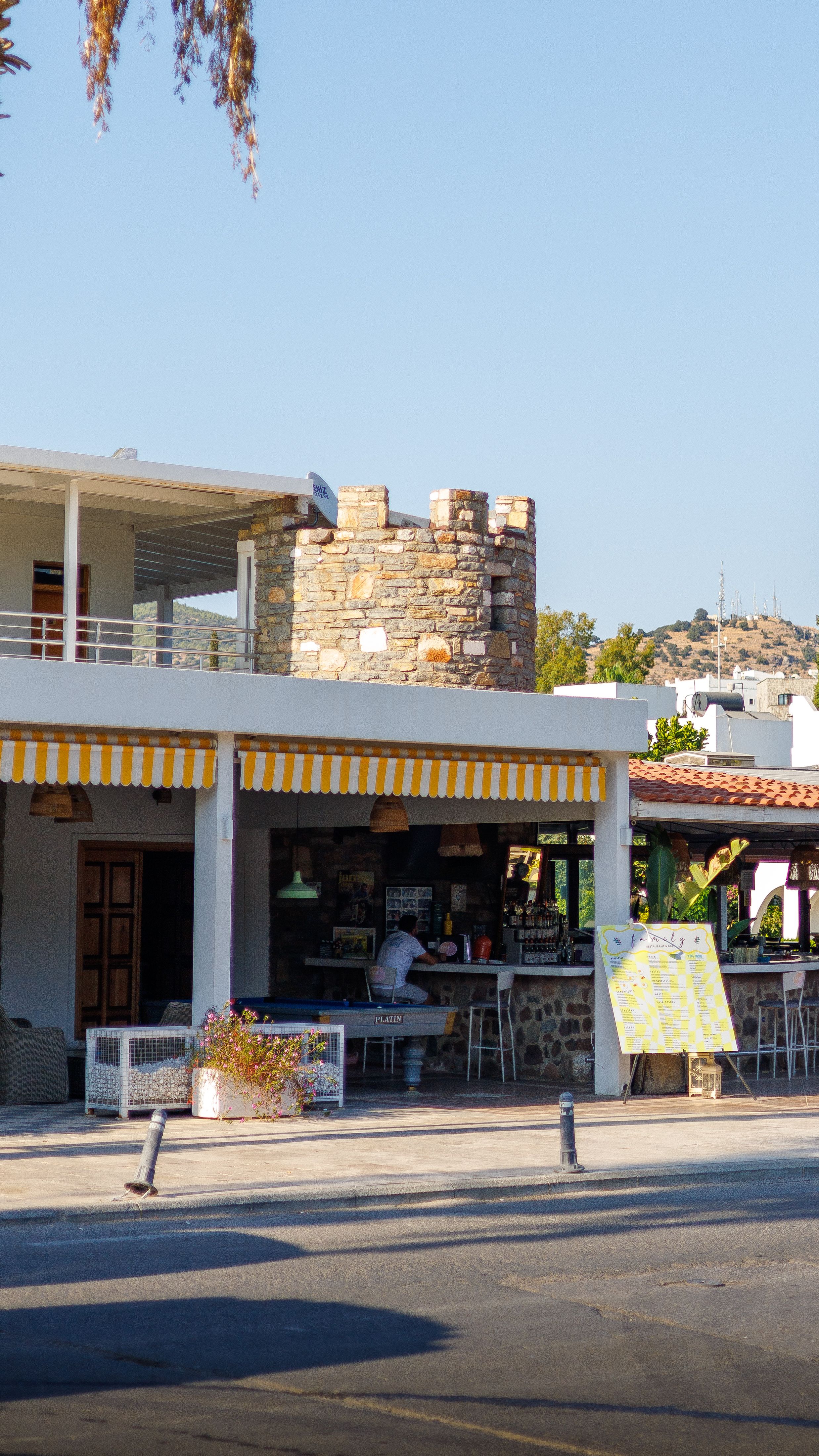 Cozy outdoor cafe with yellow striped awning next to historical stone tower.