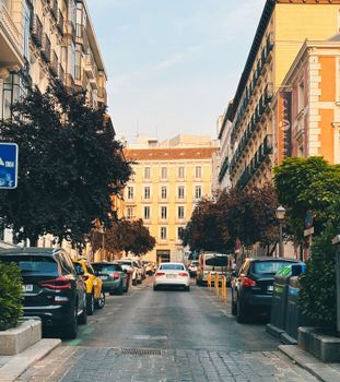 A scenic European street lined with parked cars and lush trees, evoking urban charm.