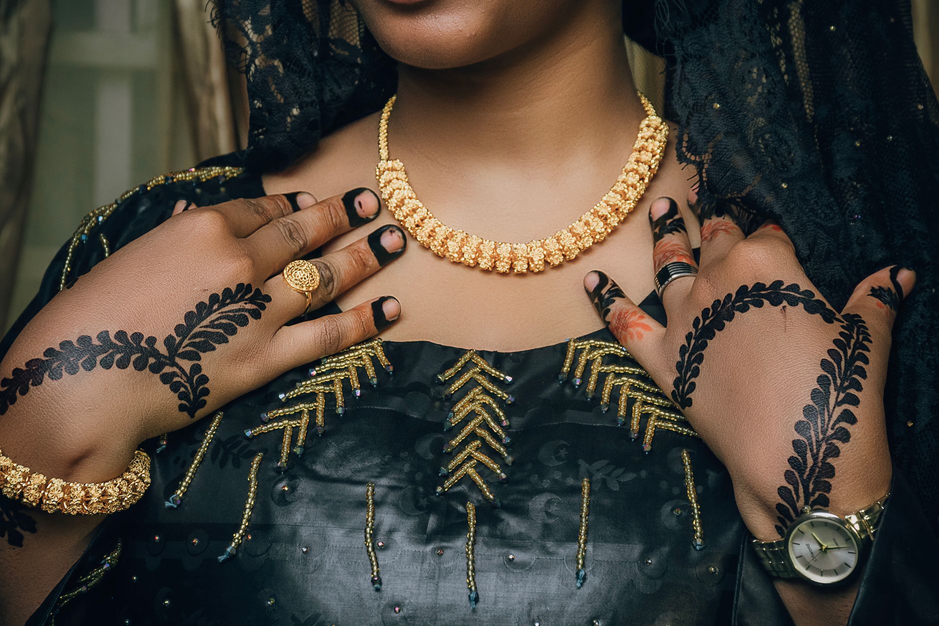 Close-up of henna-adorned hands with gold jewelry on dark fabric, exuding elegance.