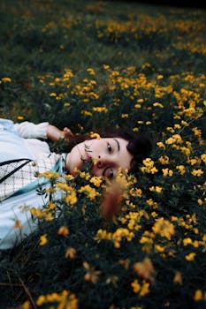 A woman lies in a field of yellow flowers, creating a moody and serene scene.