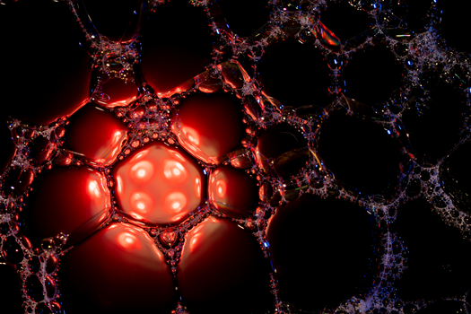 Close-up of soapy bubbles with red and black highlights, showcasing a dramatic abstract texture.
