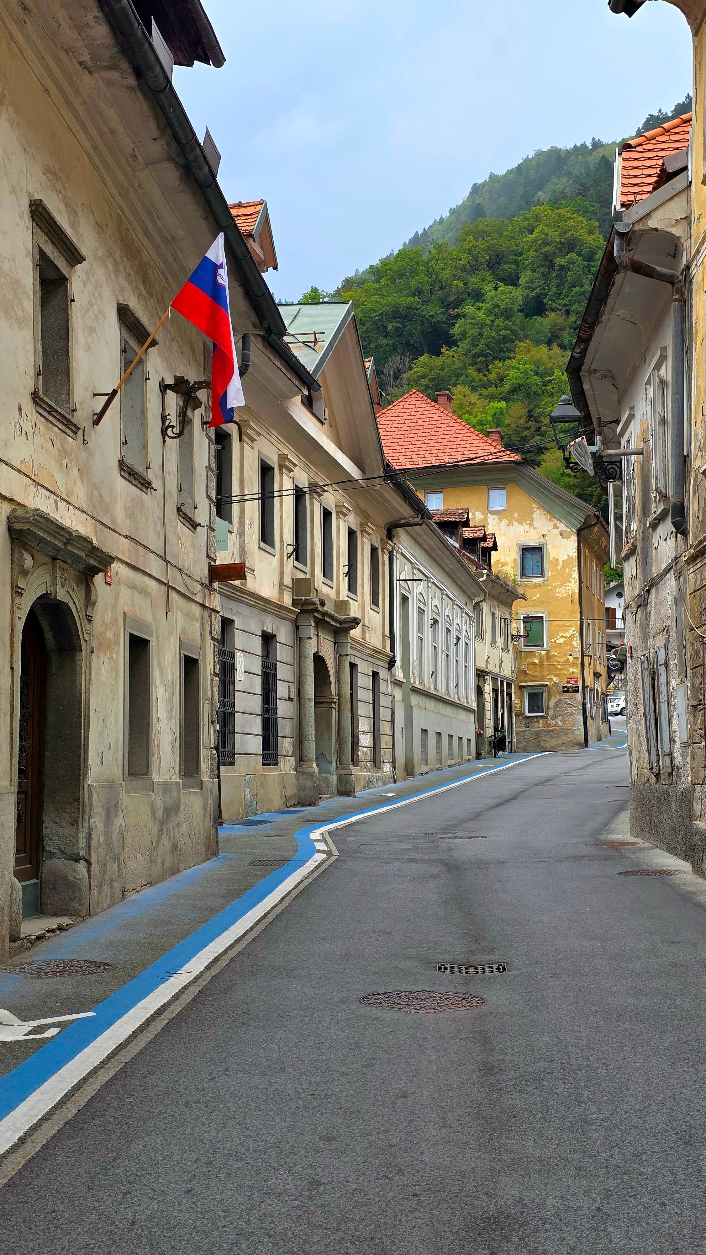 Charming view of a quiet historic street adorned with a Slovenian flag, nestled in a mountainous European town.