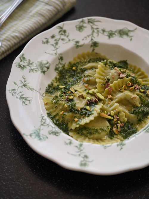 Free Plate of spinach ravioli topped with pesto and crushed nuts in floral-patterned dish. Stock Photo