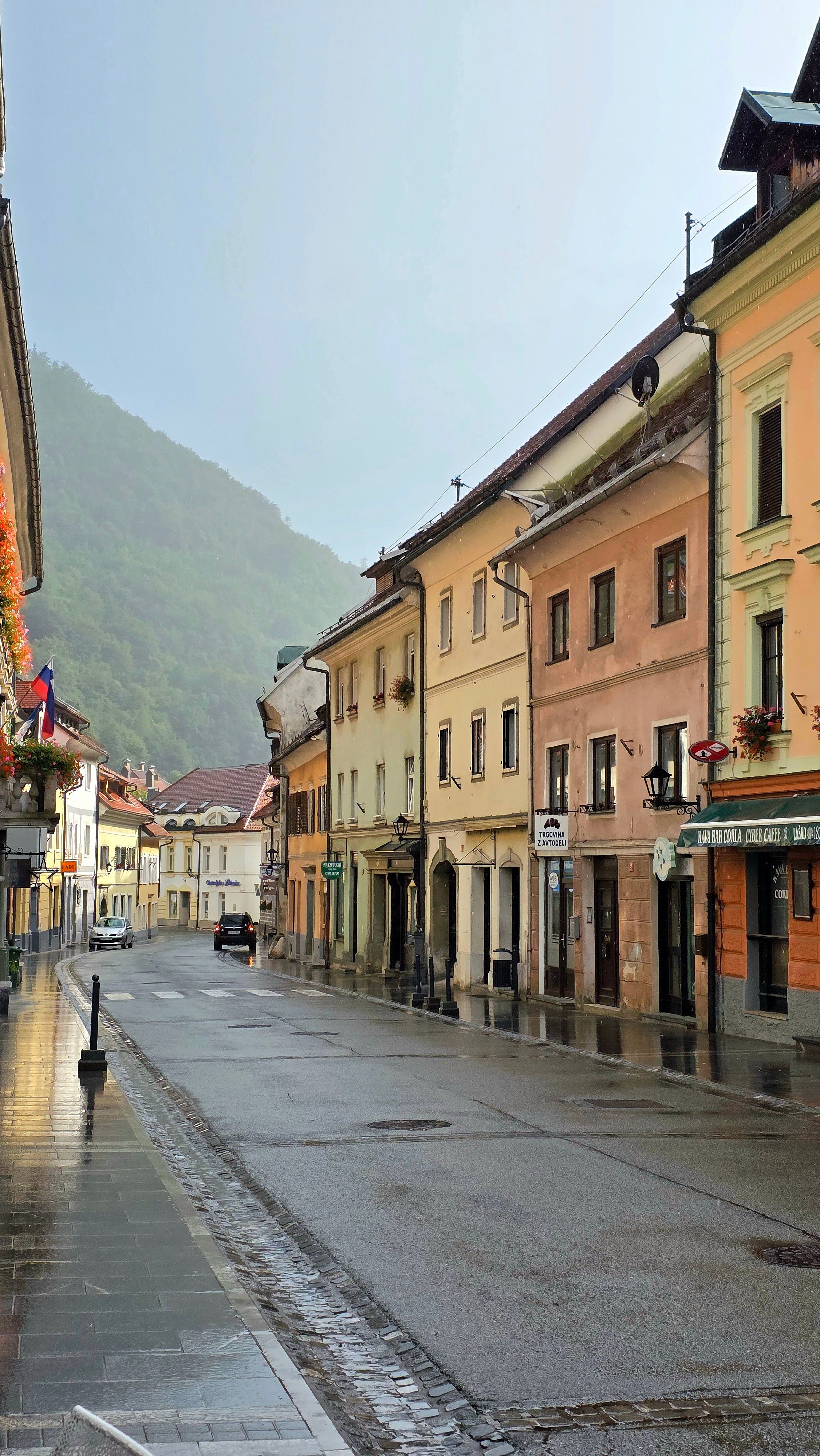 Quiet European street with colorful buildings and wet pavement after a rainfall, nestled by hills.