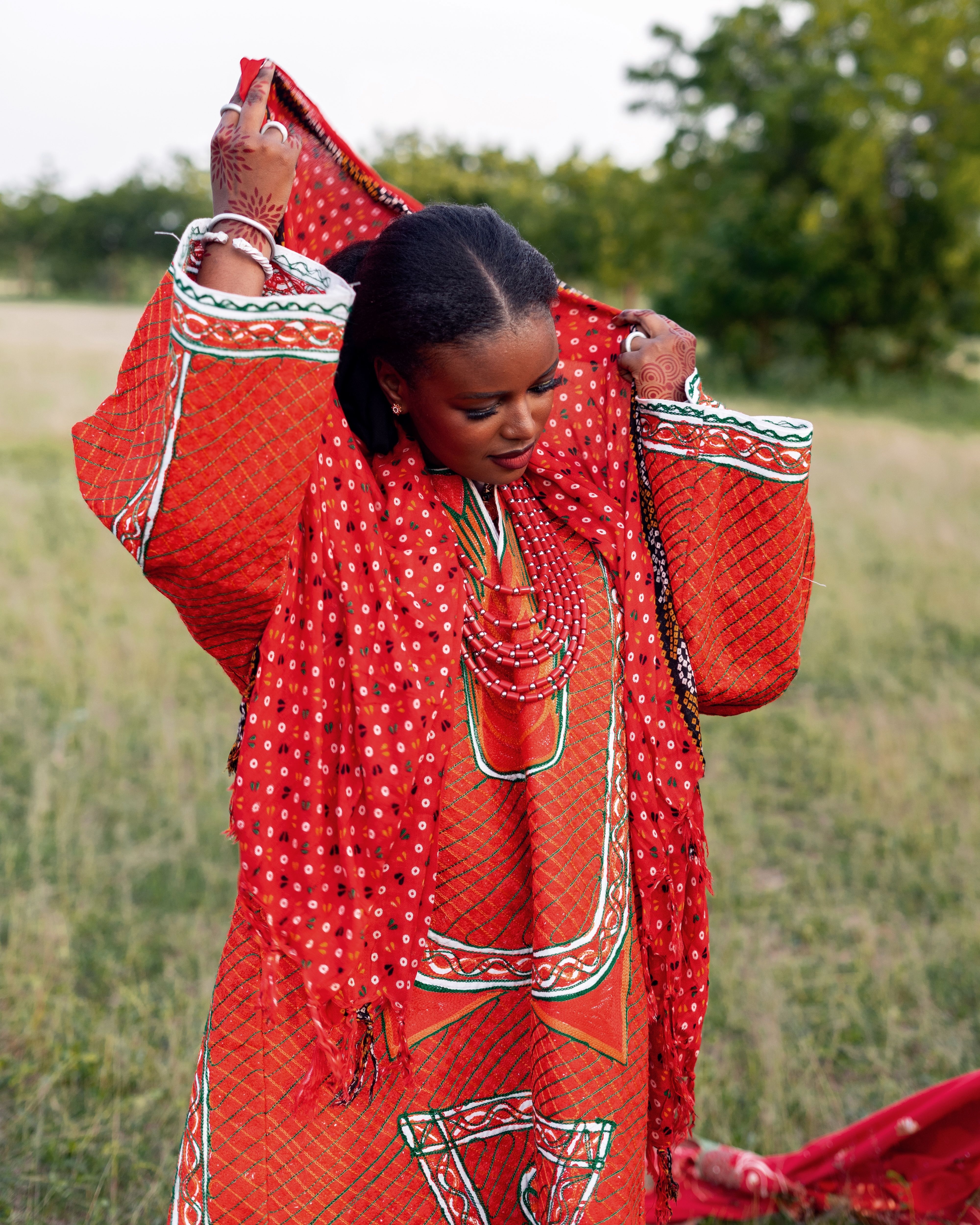 A woman draped in vibrant traditional Nigerian attire in a lush outdoor setting.