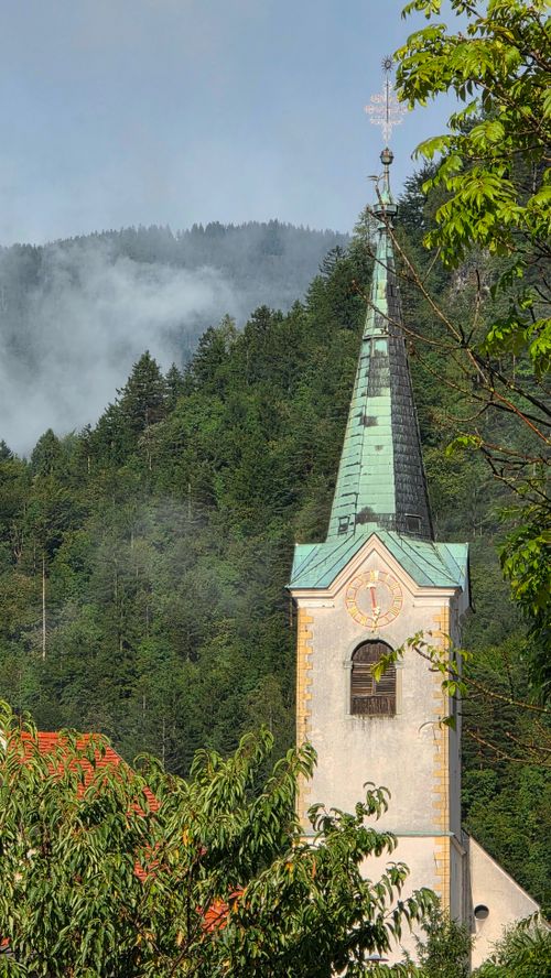 Free Picturesque church steeple amid lush Alps, against a misty mountain backdrop. Stock Photo