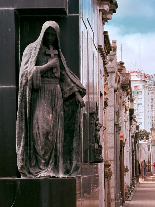 Free Dramatic gothic statue in Recoleta Cemetery, Buenos Aires captures historic art with modern city backdrop. Stock Photo