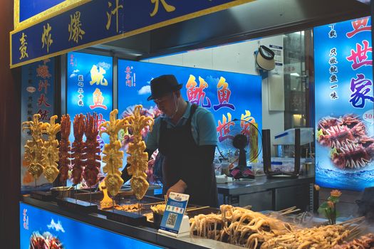 Night market vendor selling skewered food in Beijing, China, with vibrant signage and lively atmosphere.
