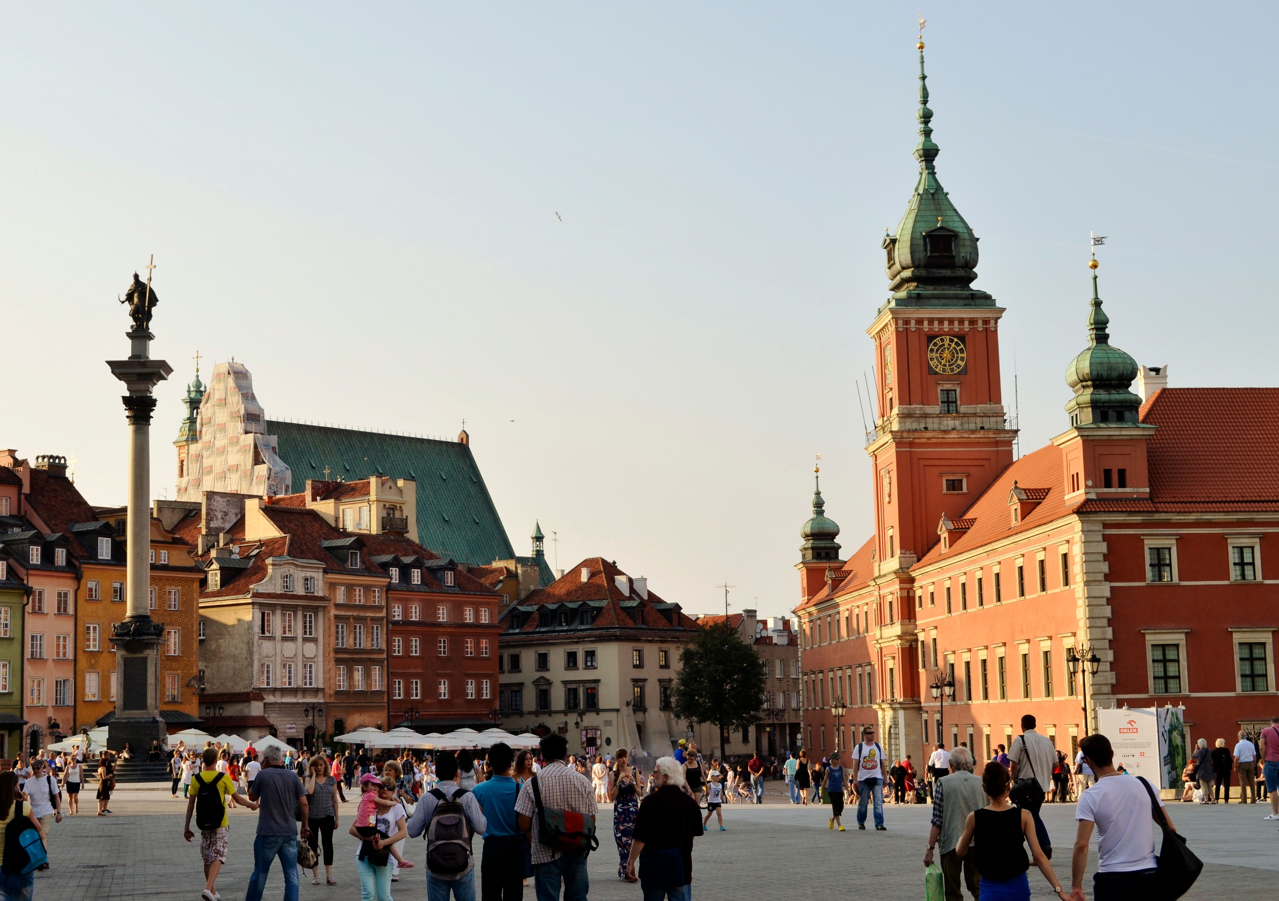 Lively scene in Warsaw's Old Town Square featuring Sigismund's Column and the Royal Castle tower.