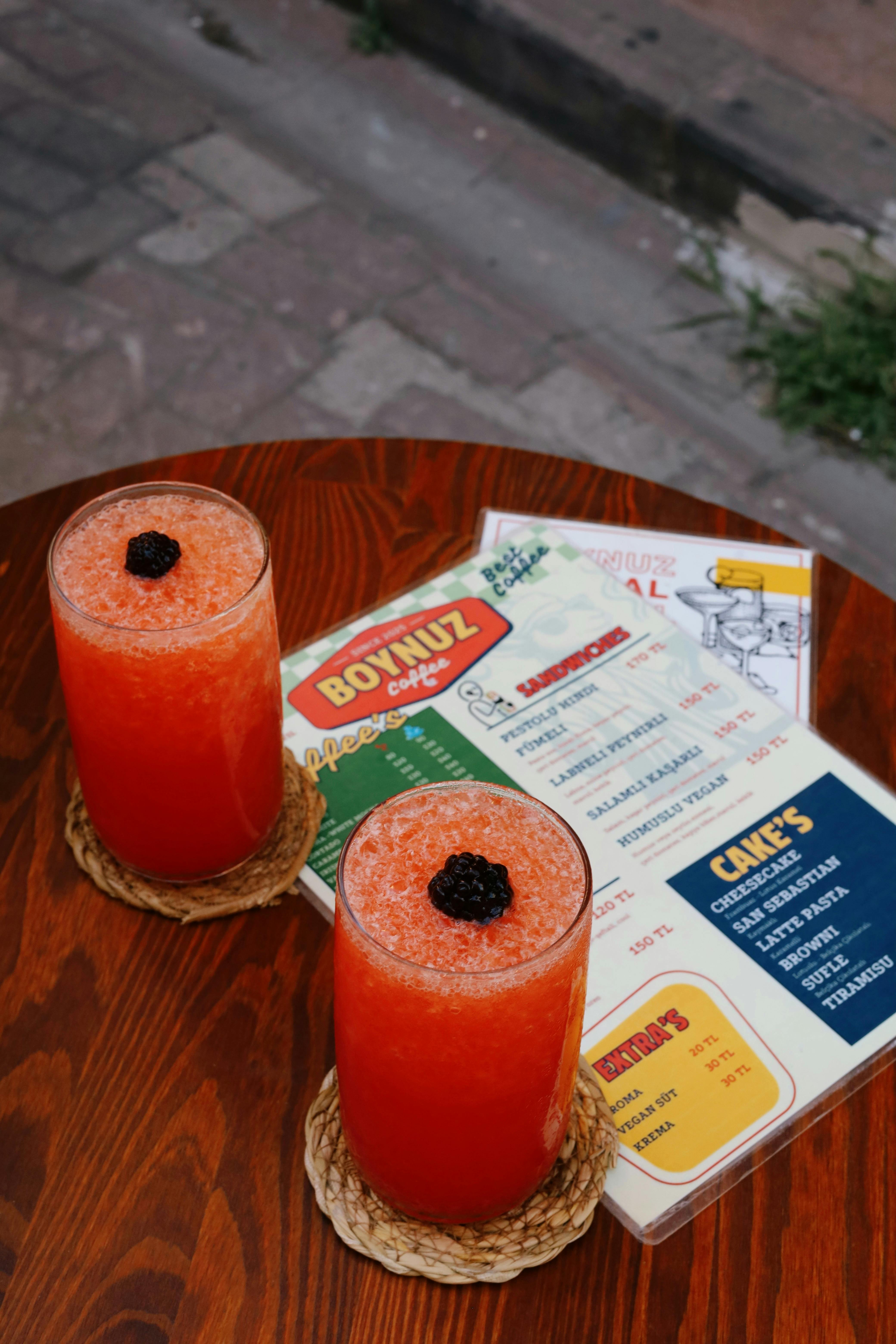 Vibrant orange drinks on a wooden table at an outdoor café, featuring menus for close-up detail.