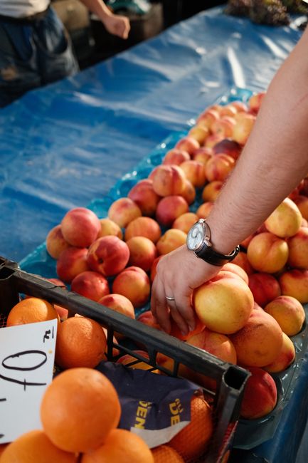 A person picks fresh peaches at a vibrant outdoor market stall.