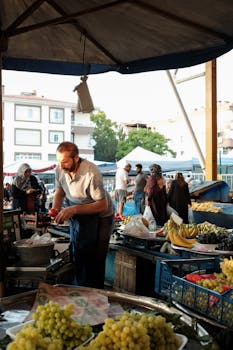 Outdoor market bustling with people shopping for fresh fruits and vegetables under a canopy.