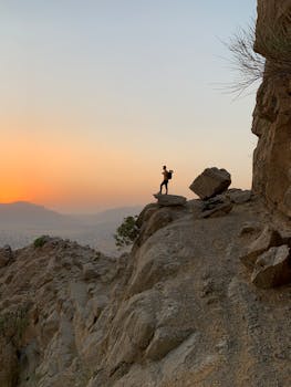 岩石悬崖上，日出时站立的人的剪影，捕捉了户外冒险的宁静时刻