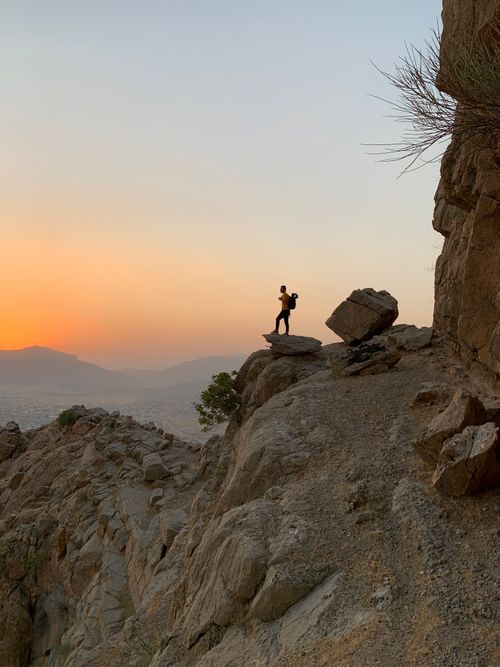 Free Silhouette of a person standing on a rocky cliff during sunrise, capturing a serene outdoor adventure moment. Stock Photo