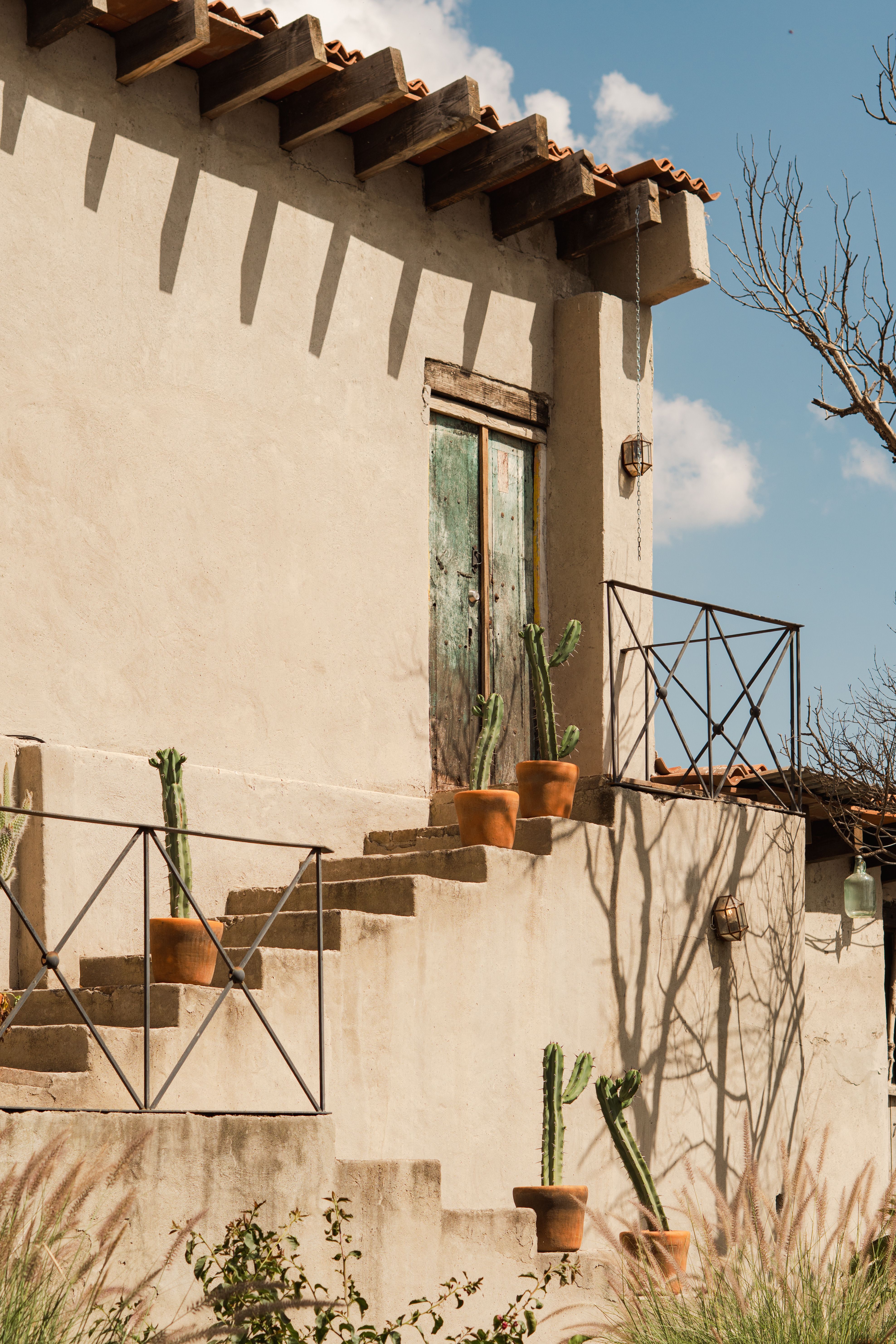 Gratis Affascinante esterno rustico di una casa in adobe con cactus in vaso, immortalato nella calda luce del sole. Perfetto per immagini di viaggio o lifestyle. Foto a disposizione