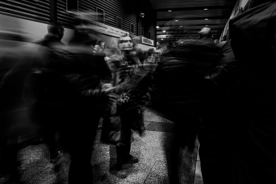 Black and white image capturing motion blur of people in a busy urban train station.